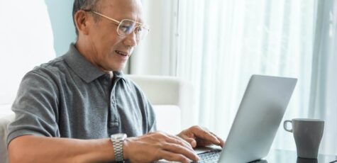 An elderly man confidently manages his pension transfer using his laptop, embracing the convenience and empowerment of digital finance